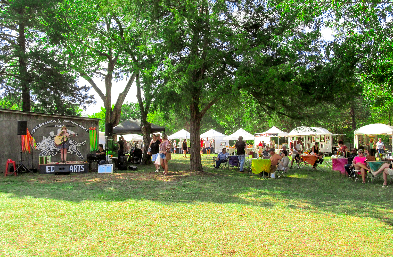 Outdoor festival with stage and vendor tents.