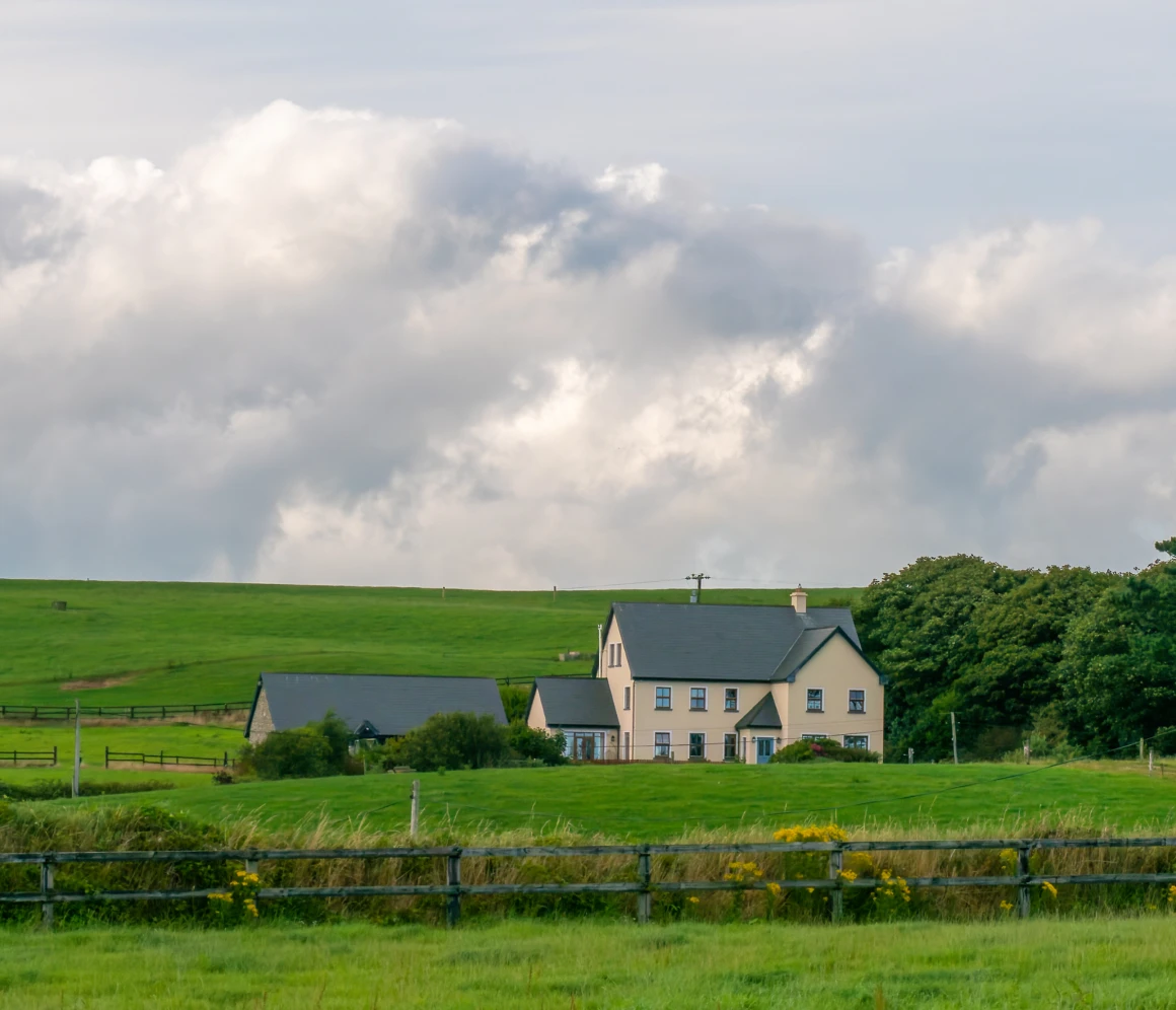 Countryside house with green fields and clouds.