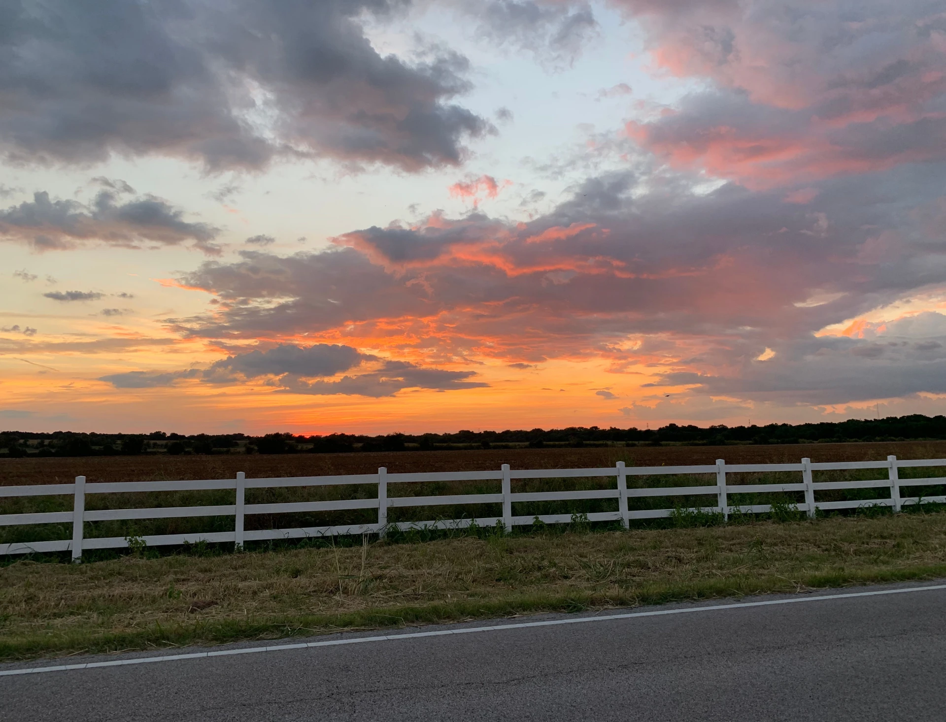 Sunset over field with white fence.